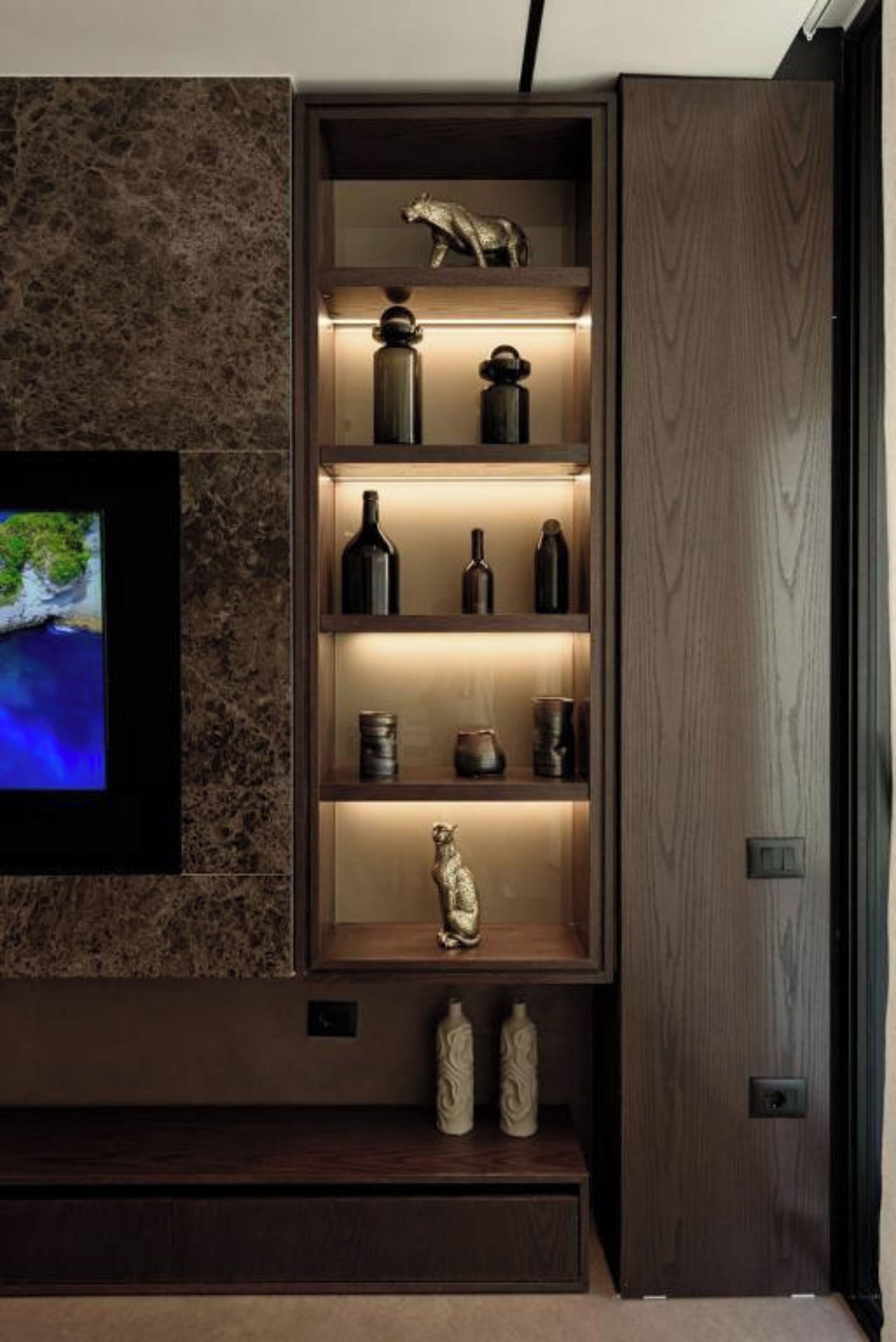Un intérieur moderne avec un meuble en bois où sont exposés divers objets décoratifs et un téléviseur fixé sur un mur en marbre.