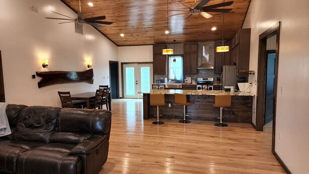 A spacious living room with a leather couch, a dining area, a kitchen with bar stools, and a ceiling fan.