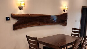 A dining area with a wooden table and chairs, a wall-mounted light fixture, and a thermostat.