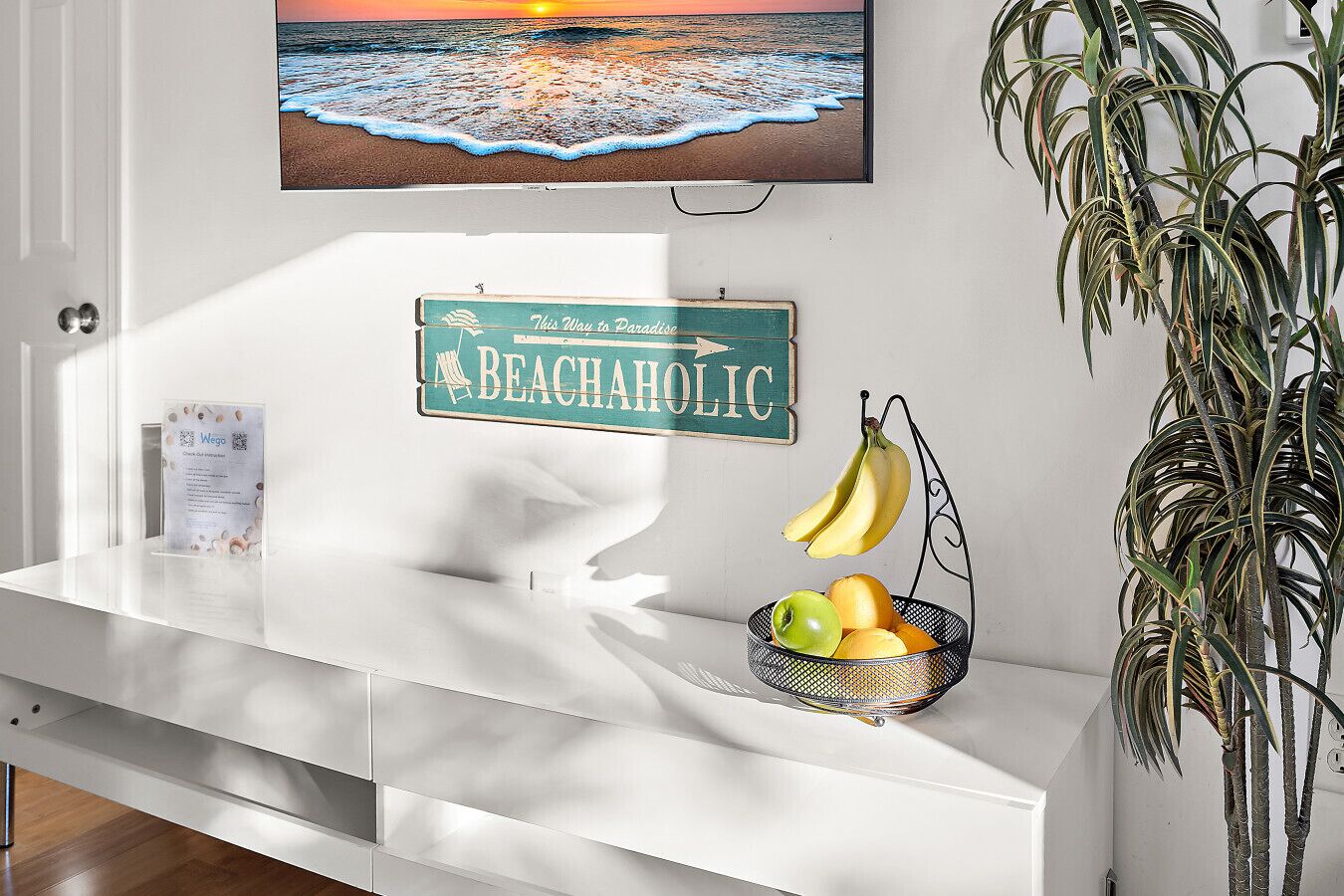 Een witte receptiebalie met een bord in strandthema, een fruitmand en een hangplant.