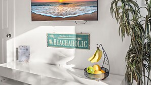 A white reception desk with a beach-themed sign, a fruit basket, and a hanging plant.