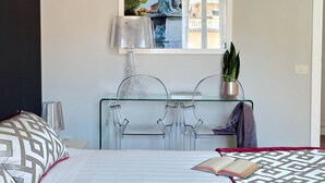 Une chambre d’hôtel avec un lit, une table en verre avec des chaises, une lampe, un tableau et une plante.