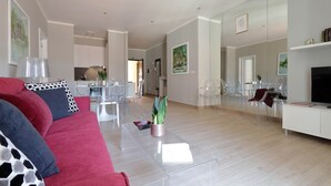 Un salon moderne avec un canapé rouge, une table basse en verre transparent et un téléviseur posé sur un meuble blanc.