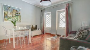 A modern living room with a glass dining table, clear chairs, a grey sofa, and a television. - Piazzetta Margutta - A3 (Rome)