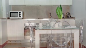 A modern kitchen with a microwave, kettle, and glass table with clear chairs. - Piazzetta Margutta - A3 (Rome)