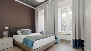 A bedroom with a bed, bedside tables, curtains, and a window with a view of greenery. - Piazzetta Margutta - B3 (Rome)