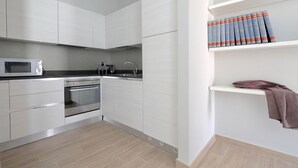 A modern kitchen with white cabinets, a microwave, an oven, and a sink. There are books on a shelf and a towel hanging on the wall. - Piazzetta Margutta - B3 (Rome)