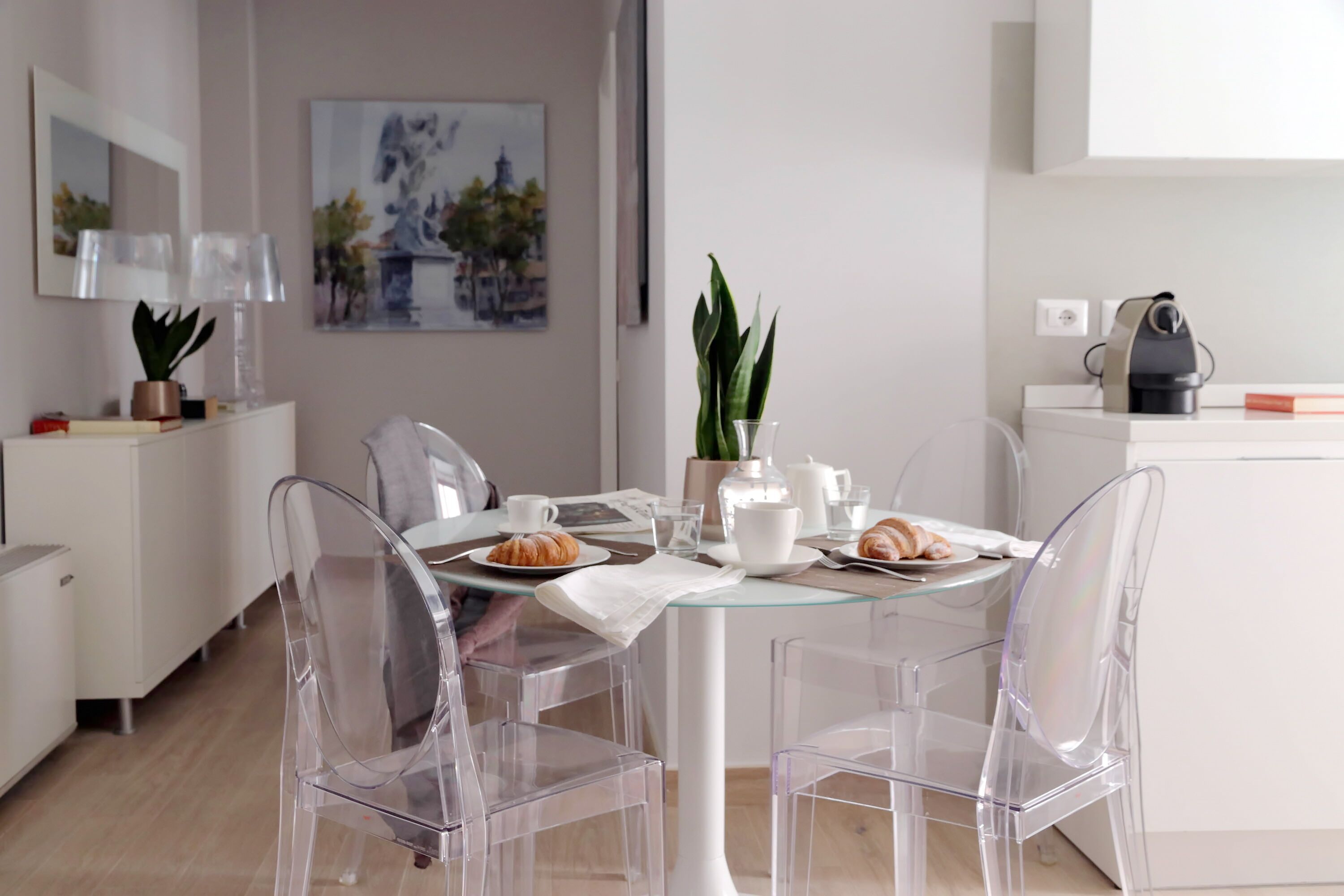 A modern dining area with a glass table, clear chairs, and a white cabinet.