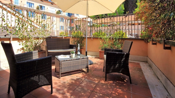 Een terras buiten met rieten meubels, een tafel en een grote parasol.