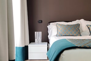 Un letto rifatto con cuscini decorati, un comodino con una lampada e un interruttore a muro.