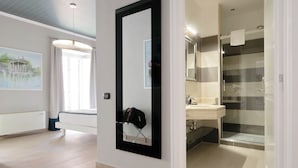 Een moderne hotelkamer met een grote spiegel, een bed, een badkamer met een douchecabine en een schilderij aan de muur.