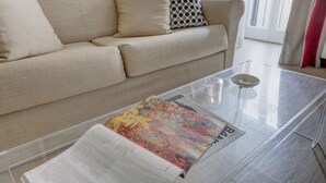 En stue med en beige sofa, et glasbord og et magasin.