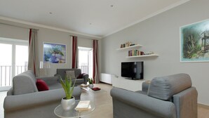 A modern living room with grey sofas, a coffee table, a TV, and a bookshelf.