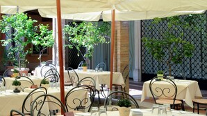 An outdoor dining area with tables set for two, surrounded by metal chairs and covered by a canopy.
