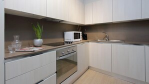 A modern kitchen with white cabinets, a built-in oven, a microwave, and a sink.