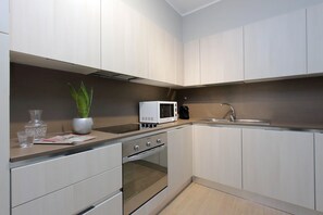 Una cocina moderna con armarios blancos, horno integrado, microondas y pileta.