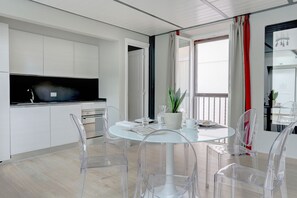 Une cuisine moderne avec des meubles blancs, un four encastré et une grande fenêtre ornée de rideaux rouges.