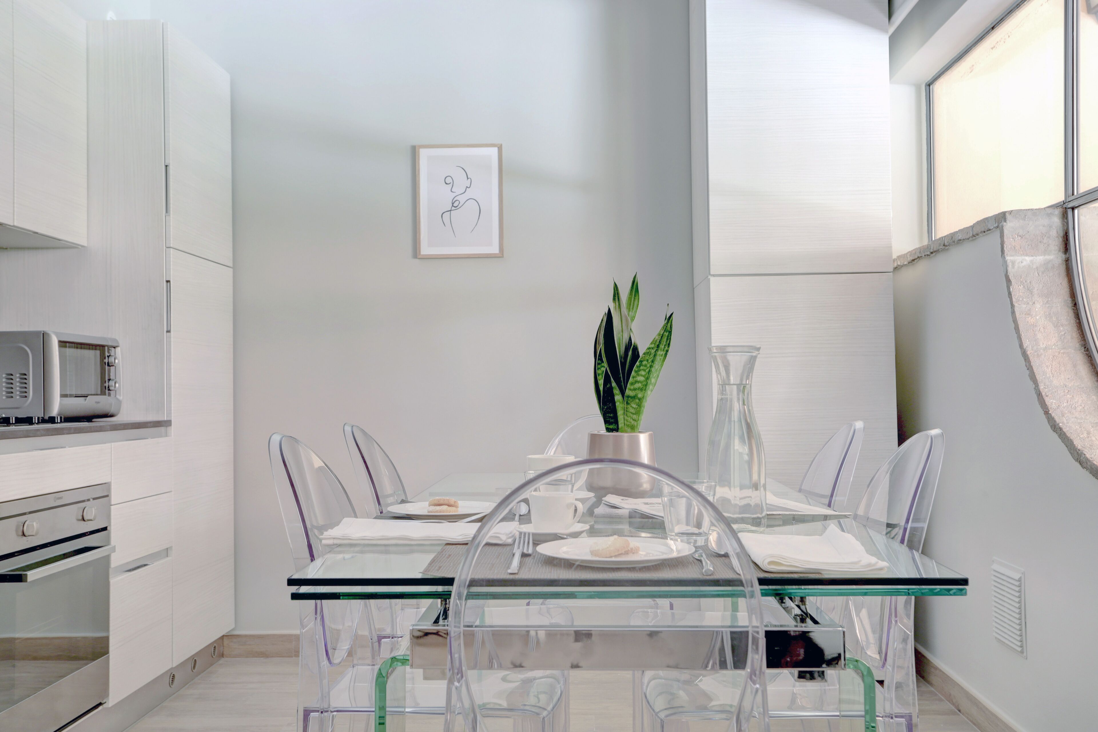 A modern kitchen with white cabinetry, a microwave, and a dining area with a glass table and clear chairs.