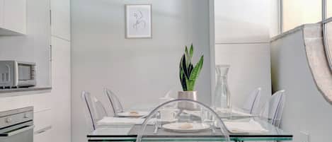 A modern kitchen with white cabinetry, a microwave, and a dining area with a glass table and clear chairs.
