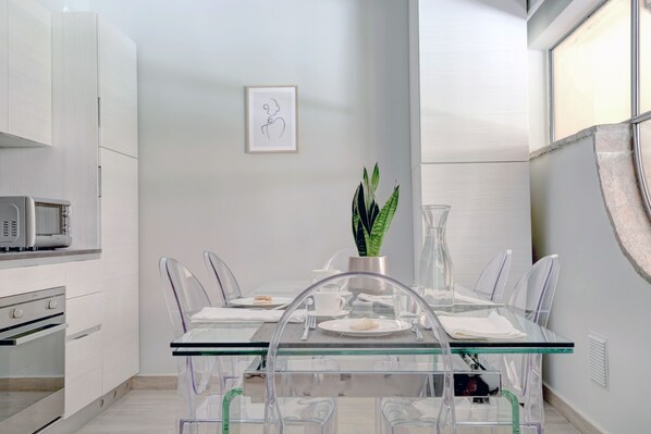 A modern kitchen with white cabinetry, a microwave, and a dining area with a glass table and clear chairs.