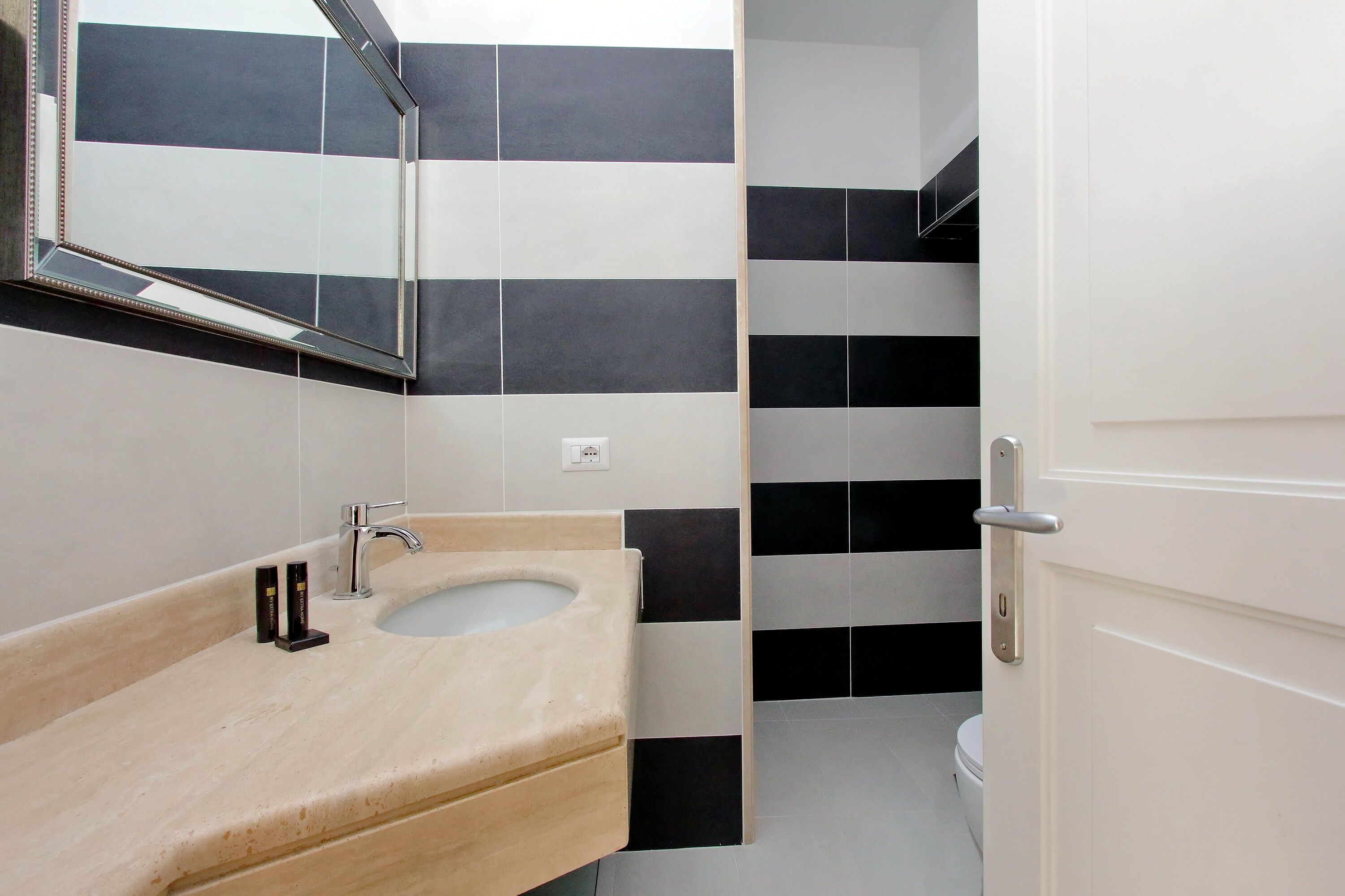 Een moderne badkamer met een beige wastafel, een spiegel en zwart-wit gestreepte tegels.