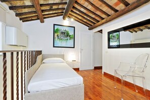 A bedroom with a bed, wooden ceiling beams, a framed picture, and a clear chair.