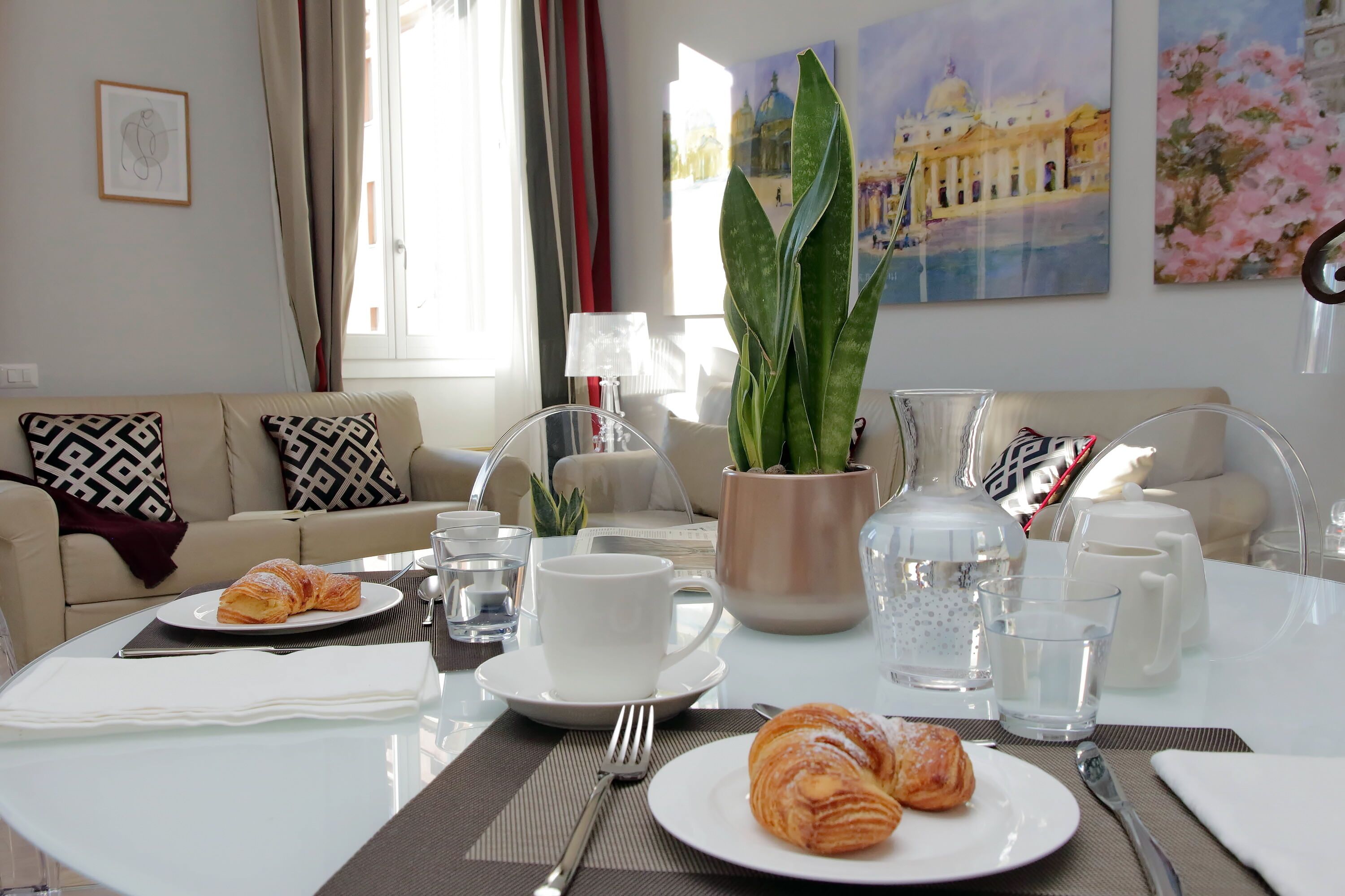 A dining area with a table set for breakfast, including croissants, a cup, and a pitcher.
