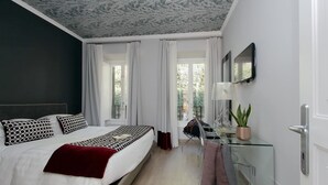 Ein modernes Schlafzimmer mit Bett, Schreibtisch, Stuhl und einer Zimmerpflanze.