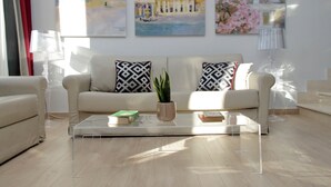 Ein modernes Wohnzimmer mit einem beigen Sofa, gemusterten Kissen, einem Glastisch und einer Topfpflanze.