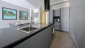 Una cocina moderna con una isla central, pileta de acero inoxidable y muebles grises. Hay dos cuadros enmarcados en la pared, un microondas y una puerta que da a otra habitación.