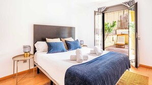 A modern hotel room with a large bed, a bedside table with a lamp, and a view of a balcony with plants. - Pl Universitat Comfortable 3BD with private patio (Barcelona)