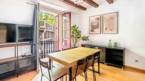 A dining area with a wooden table and chairs, a TV on a stand, and a plant. - Pl Universitat Comfortable 3BD with private patio (Barcelona)
