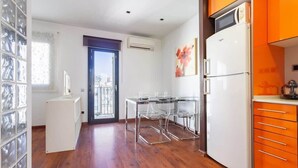 A compact kitchen with a refrigerator, a dining table with chairs, and a window with a view of buildings. - Sunny Atico with Terrace in Pl Universitat! (Barcelona)