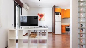 A modern kitchen with white cabinets, a microwave, and a refrigerator. There is a white console table with a television and a bowl. - Sunny Atico with Terrace in Pl Universitat! (Barcelona)
