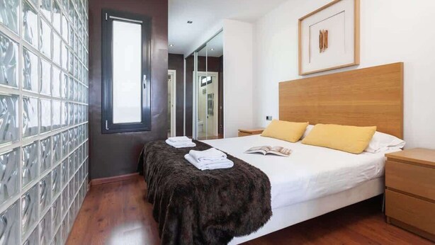 A modern hotel room with a large bed, a wooden headboard, and a glass block wall. - Sunny Atico with Terrace in Pl Universitat! (Barcelona)