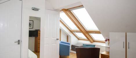 A modern, well-lit room with a skylight, a bed, a desk, and a chair.