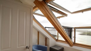 Une pièce avec un plafond en pente, une vue sur la mer, une chaise bleue et une petite boîte de rangement.