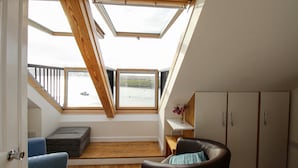 Une pièce avec un plafond en pente, des fenêtres de toit, un banc en bois, une chaise et une armoire.