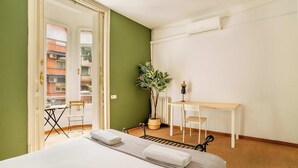Une chambre avec un lit, un bureau, une chaise, une plante en pot et une vue sur le balcon extérieur.