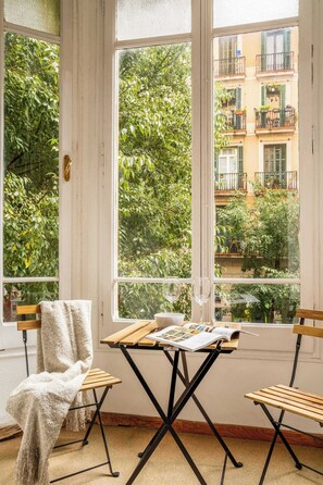 A room with a large window, a wooden table with a magazine, and two chairs. - The Collection - Historic 5BD with Private Terrace (Barcelona)