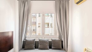 Ein Schlafzimmer mit einem Bett, grauen Vorhängen und einem Fenster mit Blick auf Gebäude.