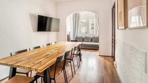 Ein moderner Essbereich mit einem langen Holztisch und Stühlen, einem an der Wand befestigten Flachbildfernseher und Blick auf einen Balkon mit einer Sitzecke.