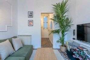 A living room with a green sofa, a wooden coffee table, a TV, and a large potted plant.