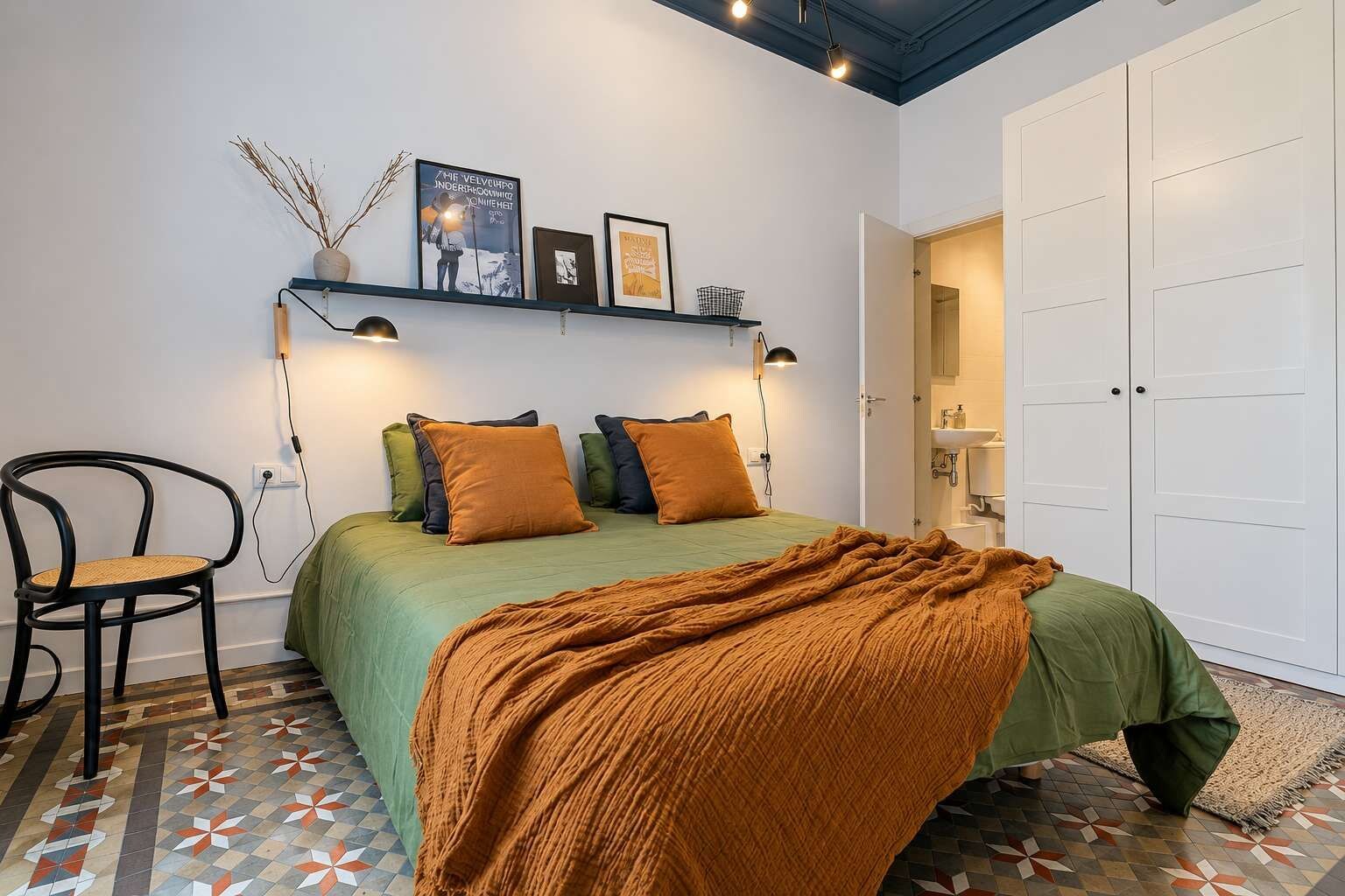 A bedroom with a bed, a chair, a shelf with pictures, and a wardrobe.