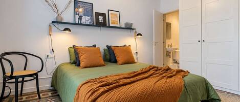 A bedroom with a bed, a chair, a shelf with pictures, and a wardrobe.