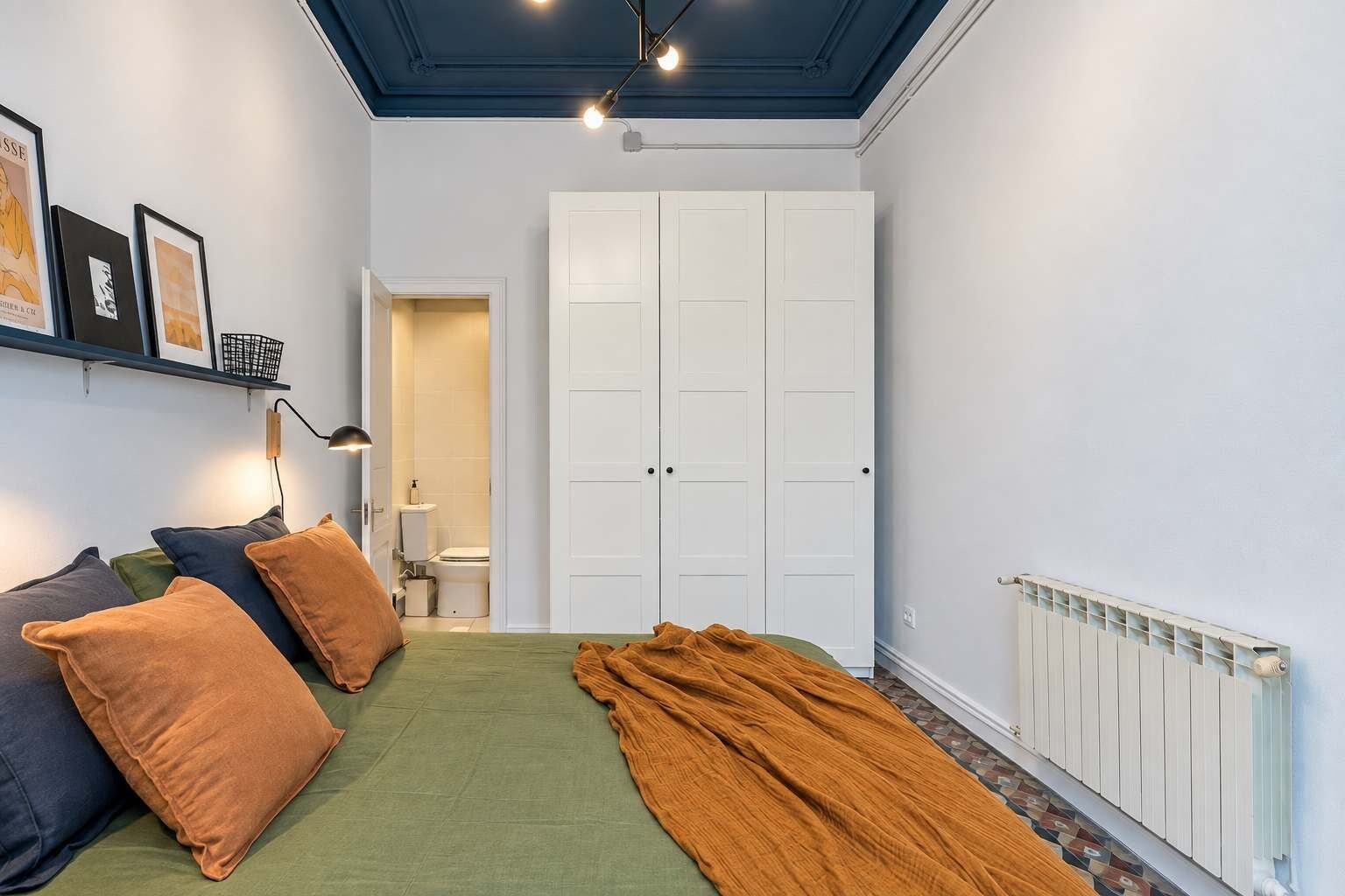 A bedroom with a bed, pillows, a radiator, and a wardrobe.