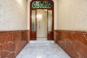 A hallway with marble flooring, a wooden door with glass panels, and decorative wall patterns. - The Collection - 4BD 3BTH with balcony in Eixample (Barcelona)