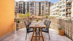 A patio with a wooden table and chairs, surrounded by a bamboo fence, overlooking a residential area with multi-story buildings. - Historic apartment with private terrace in Example (Barcelona)
