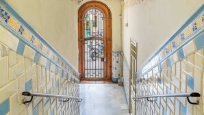 A staircase with decorative tiles and metal railings, leading to a door with a metal gate. - Historic apartment with private terrace in Example (Barcelona)