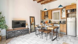 A modern kitchen with wooden cabinets, a dining table with chairs, a TV on a stand, and a large window. - Historic apartment with private terrace in Example (Barcelona)